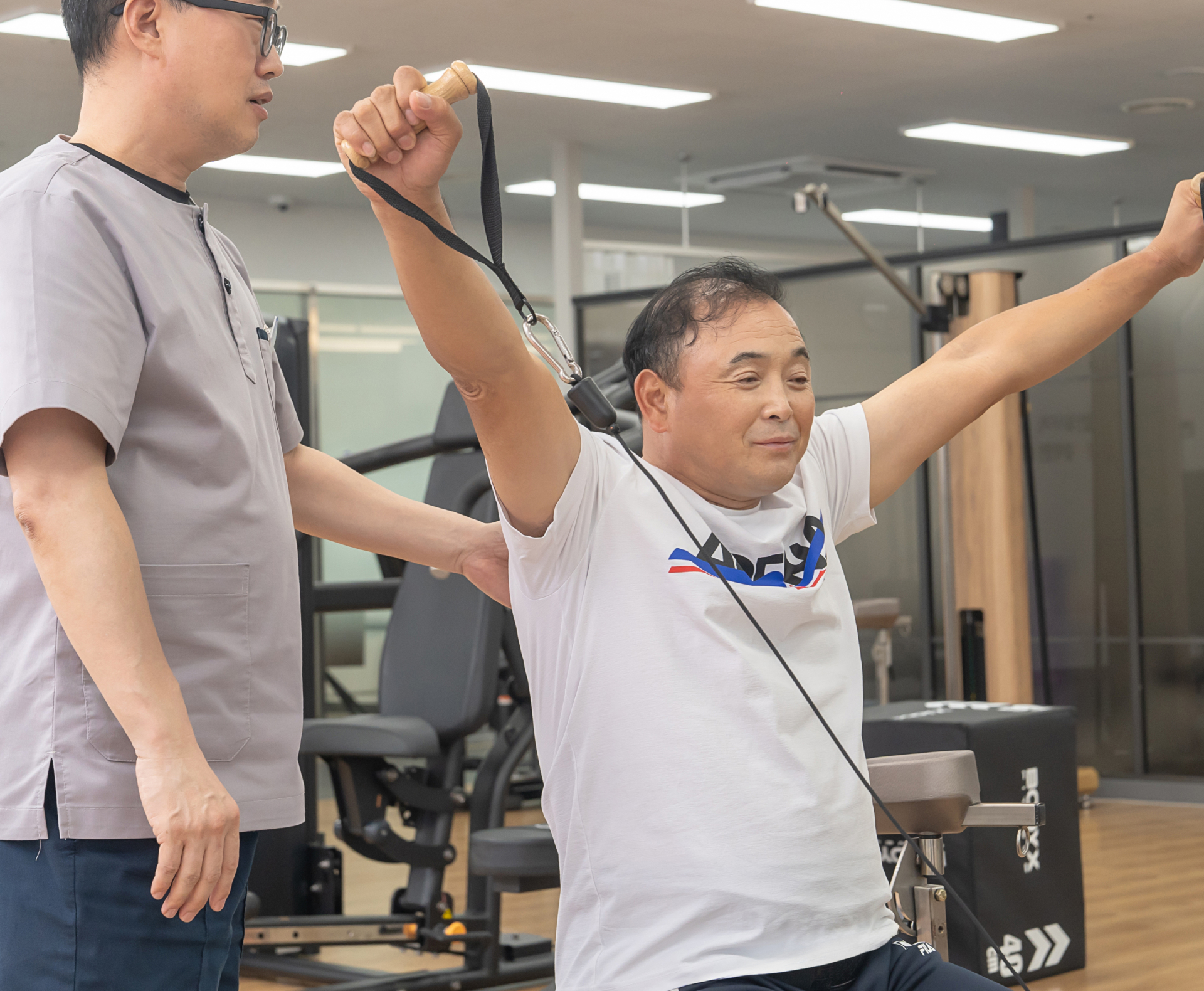 재활 트레이너와 함께 운동기구로 어깨 재활치료를 받는 환자의 모습