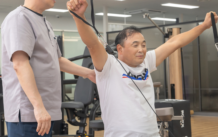 재활 트레이너와 함께 운동기구로 어깨 재활치료를 받는 환자의 모습
