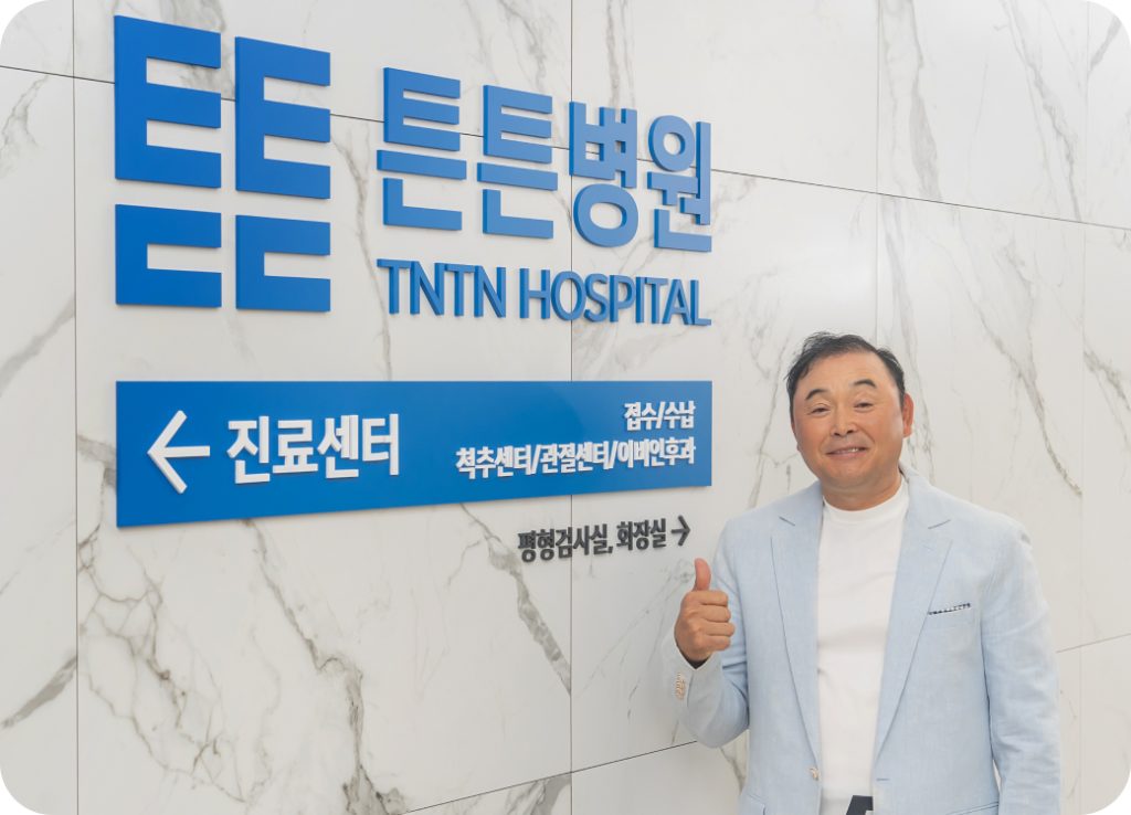 튼튼병원 TNTN HOSPITAL 안내 표지판 앞에서 엄지를 든 남성 - 진료센터(척추센터/관절센터/이비인후과), 평형검사실, 화장실 안내
